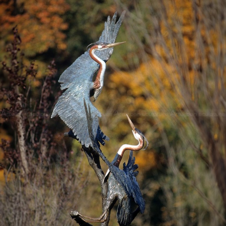 تمثالان من طيور البلشون في الهواء الطلق يقفان على غصن بأجنحة ممدودة بالكامل