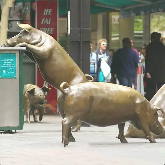 bronze A Day Out Sculpture showing one pig climbing dust bin with other pigs in the background.