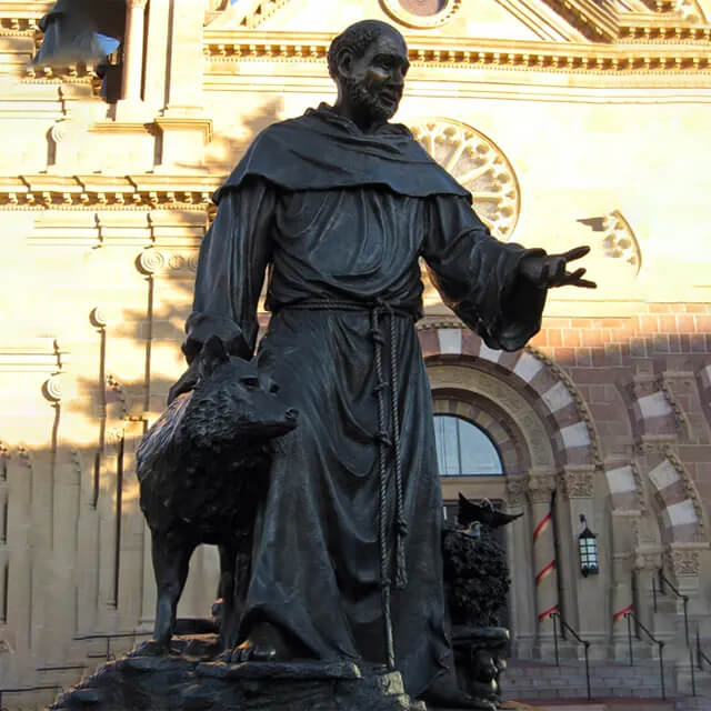 Bronze St Francis and the Wolf Statue showing the saint extending his right hand, accompanied by a calm wolf