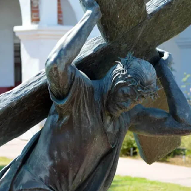 Close-up of a bronze Passion of Christ Statue showing Jesus with a crown of thorns, bearing the heavy cross on his shoulder in sorrowful expression