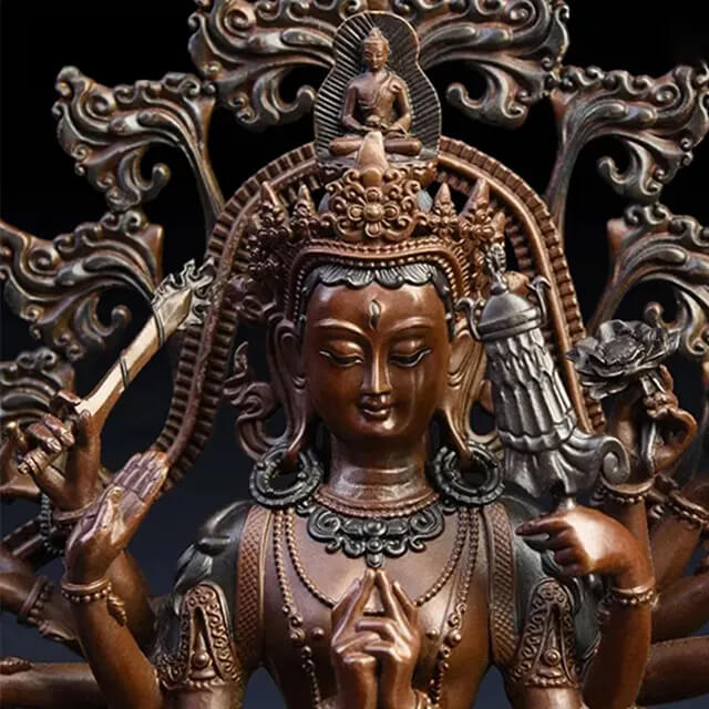 Close-up of a bronze Thousand Armed Avalokiteshvara Statue with a serene expression, multiple hands, and a small seated Buddha above the crown
