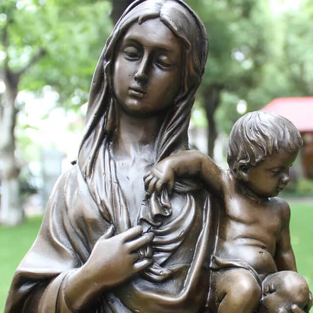 Close-up view of a bronze sculpture of Mother Mary tenderly holding baby Jesus, with a serene and peaceful expression