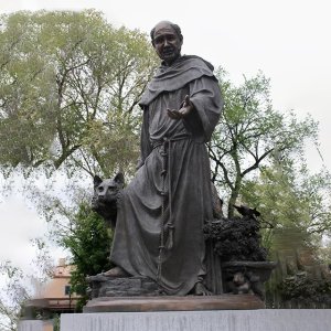 bronze St Francis and the Wolf Statue depicting St. Francis with an outstretched hand and a wolf beside him