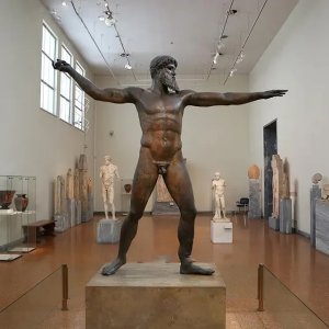 Artemision Bronze Sculpture viewed from the front right, showing a powerful ancient Greek god figure in a dynamic pose with arms extended