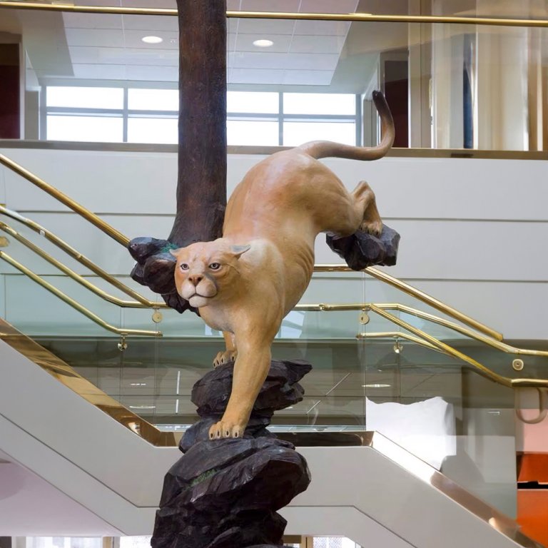 Grande statua di bronzo di un Cougar realistico che scende da un albero con espressione concentrata e movimento dinamico