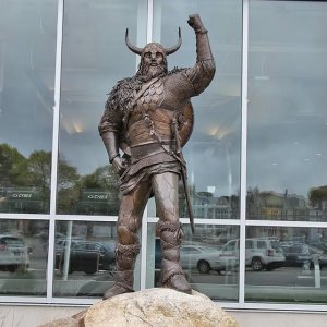 Viking Garden Statue standing triumphantly on a rock, with one arm raised and a round shield on his back