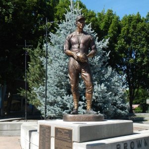 Full-body bronze Coach Statue of Don Requa standing on a pedestal with football in hand