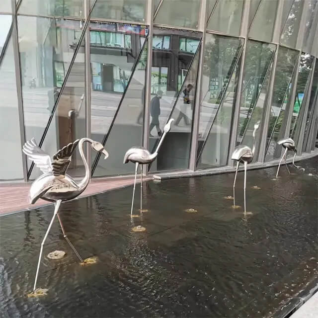 This flamingo statue outdoor sculpture group features mirror-polished stainless steel birds in lifelike walking