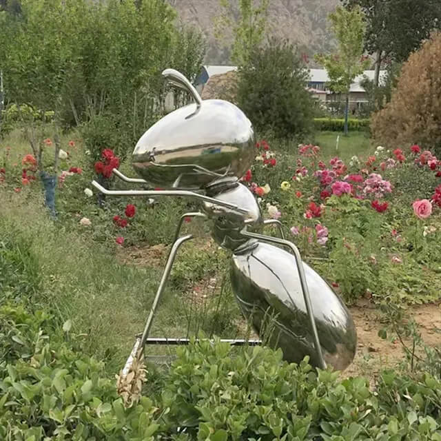 Single stainless steel ant sculpture crawling beside blooming flowers