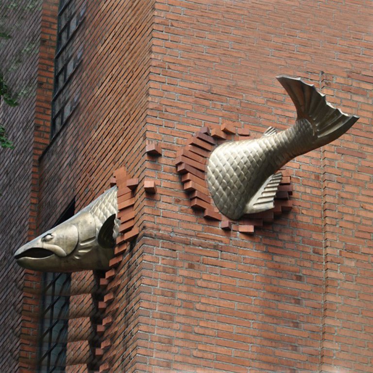 Bronze Salmon Sculpture breaking through a brick wall in Portland, created by Keith Jellum