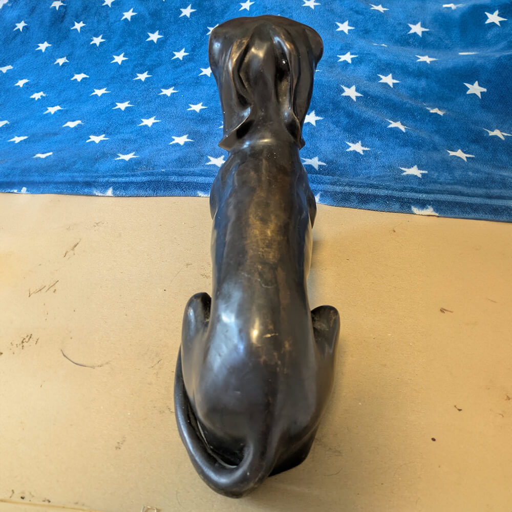 Estatua conmemorativa de perro salchicha en bronce que muestra el cuerpo alargado y la cola rizada del perro