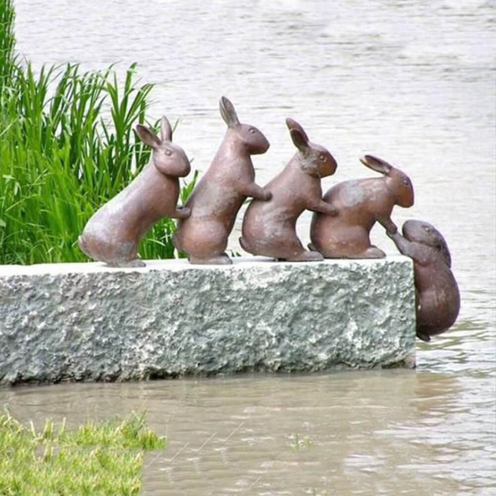 Outdoor Rabbit Sculptures in bronze showing a group of bunnies helping each other on a stone ledge
